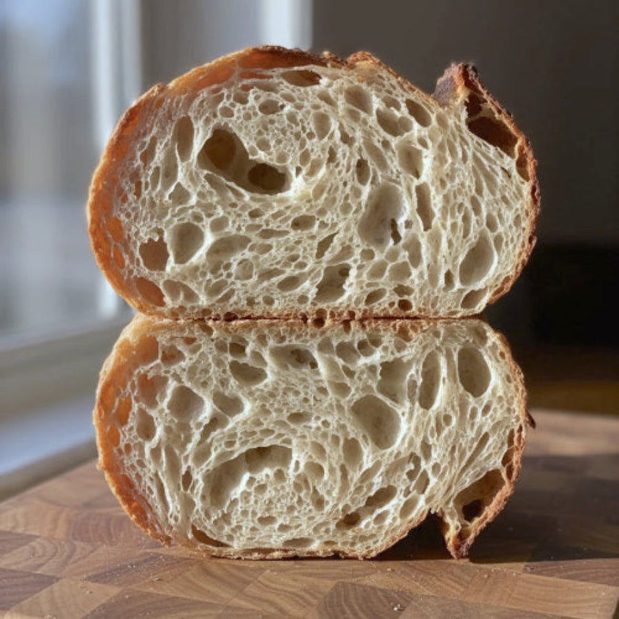 Loaf of bread cut in half on a wooden cutting board, revealing beautiful crumb