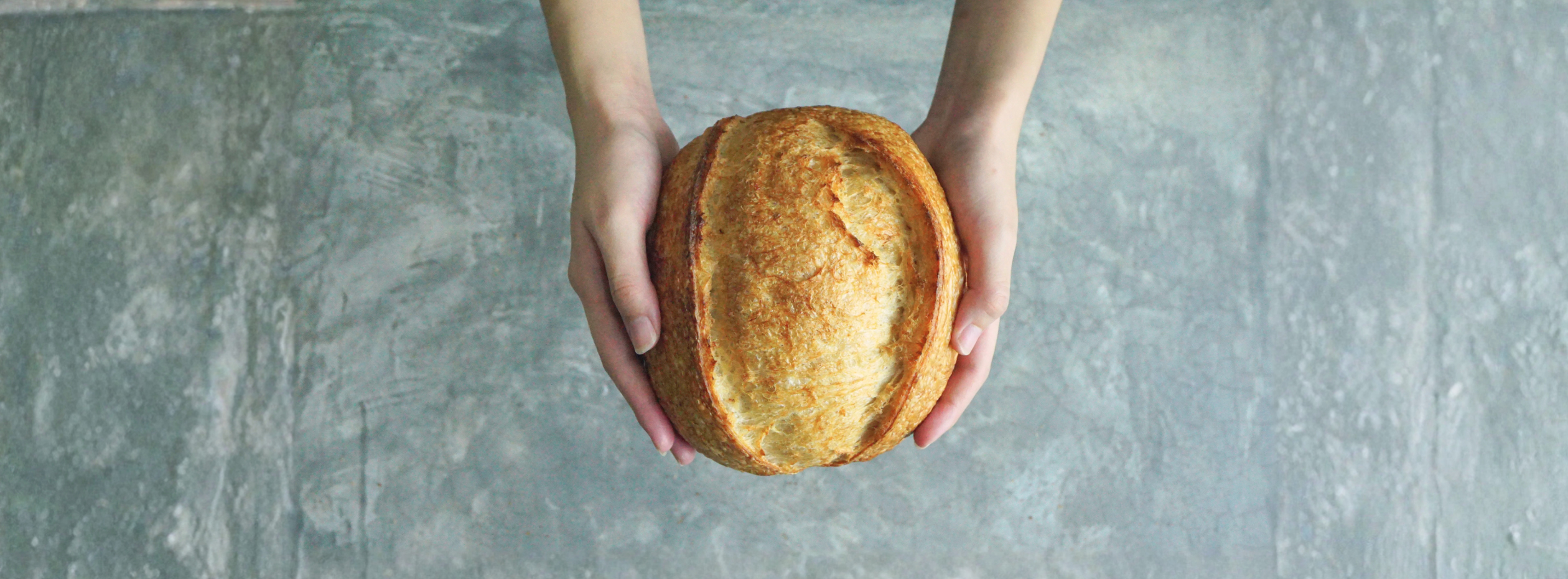 Hands holding a loaf of bread on a gray concrete surface